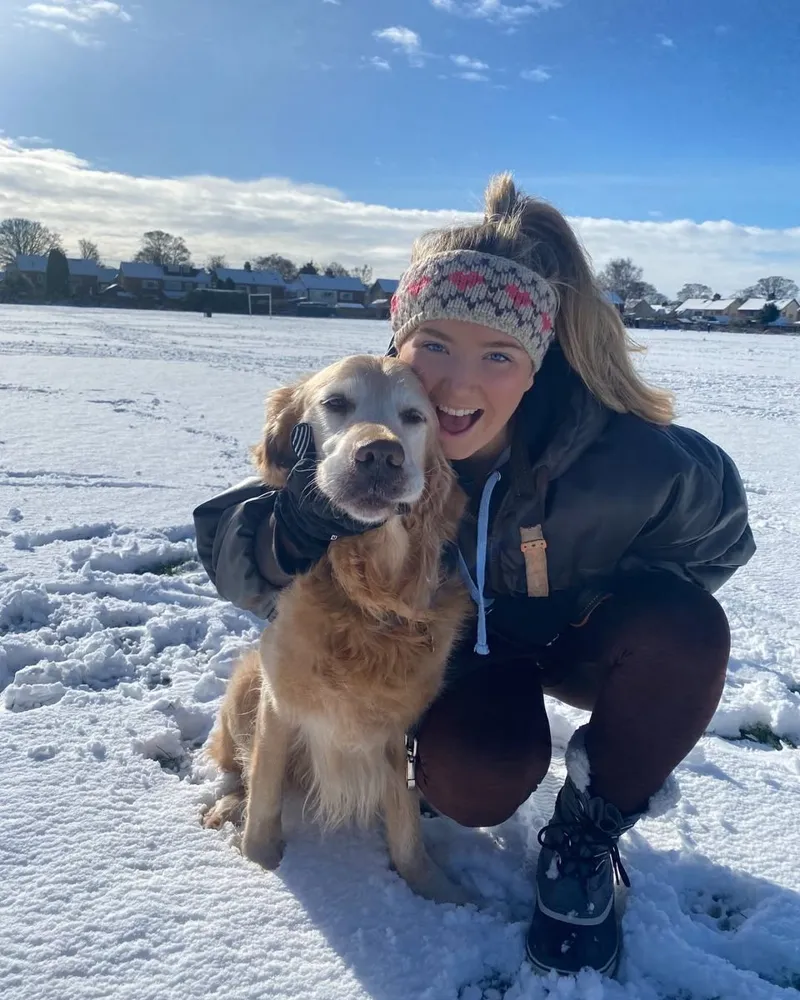 Lucy crouching in the snow with a happy golden retriever
